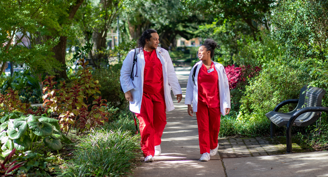 Two 鶹ҹ nursing students walking underneath a canopy of oak trees on campus