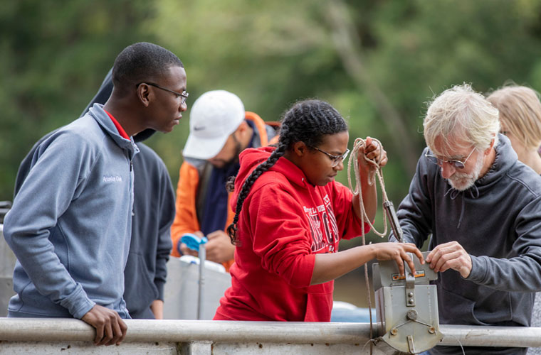 鶹ҹ biology students and faculty getting hands-on experience outside testing water samples at the river