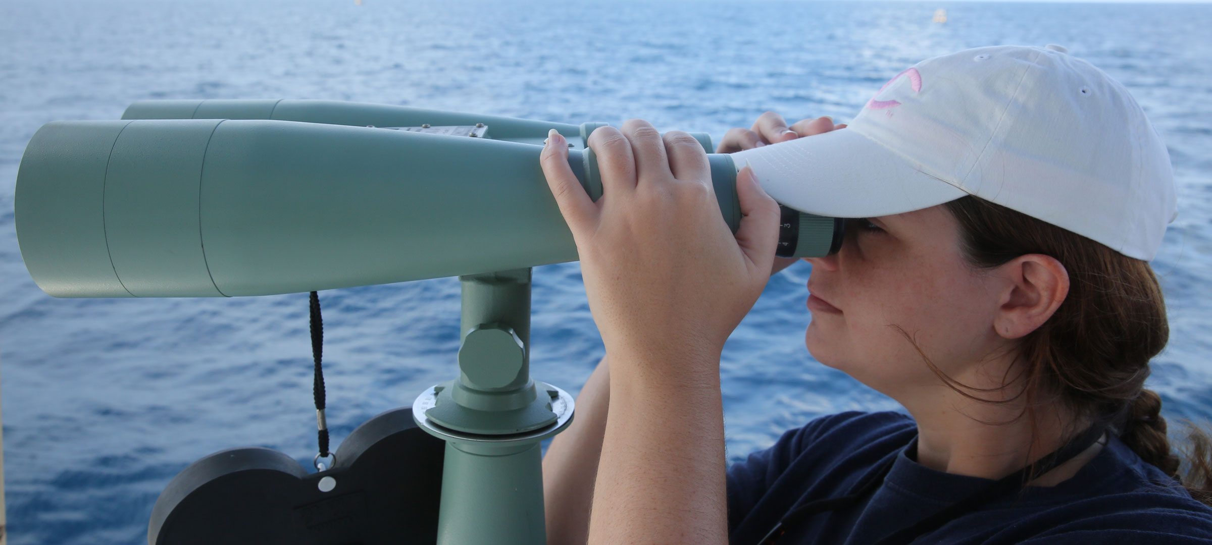 A 鶹ҹ research faculty member looks through binoculars over water during a research trip into the Gulf of Mexico