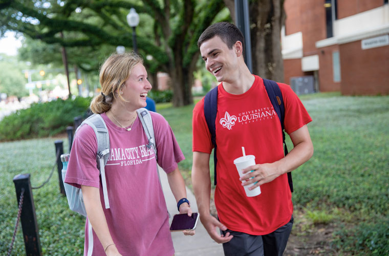 Two 鶹ҹ students smiling at each other while walking on campus