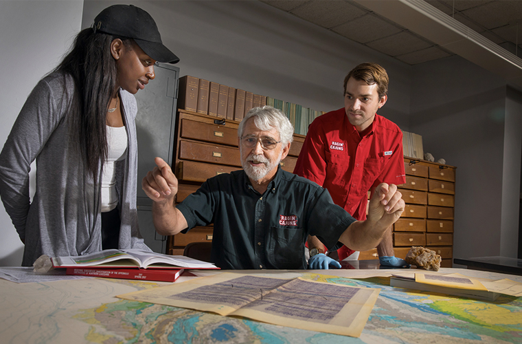 A 鶹ҹ research professor looks over maps of the coast line with two students looking over his shoulders