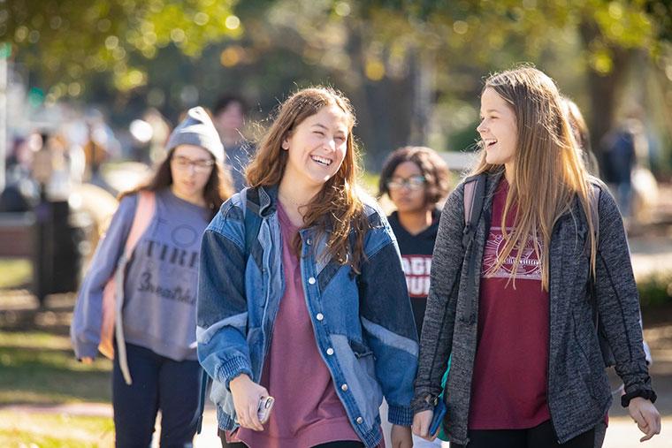 Two 鶹ҹ female students smile and laugh while walking on campus