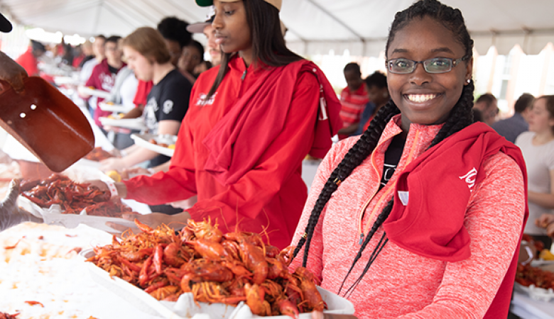 鶹ҹ student in a red pullover holding a tray of crawfish at Lagniappe Day